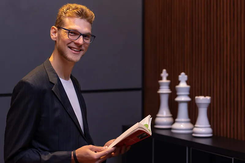 Ricardo Werlang segurando um livro, ao lado de peças de xadrez.