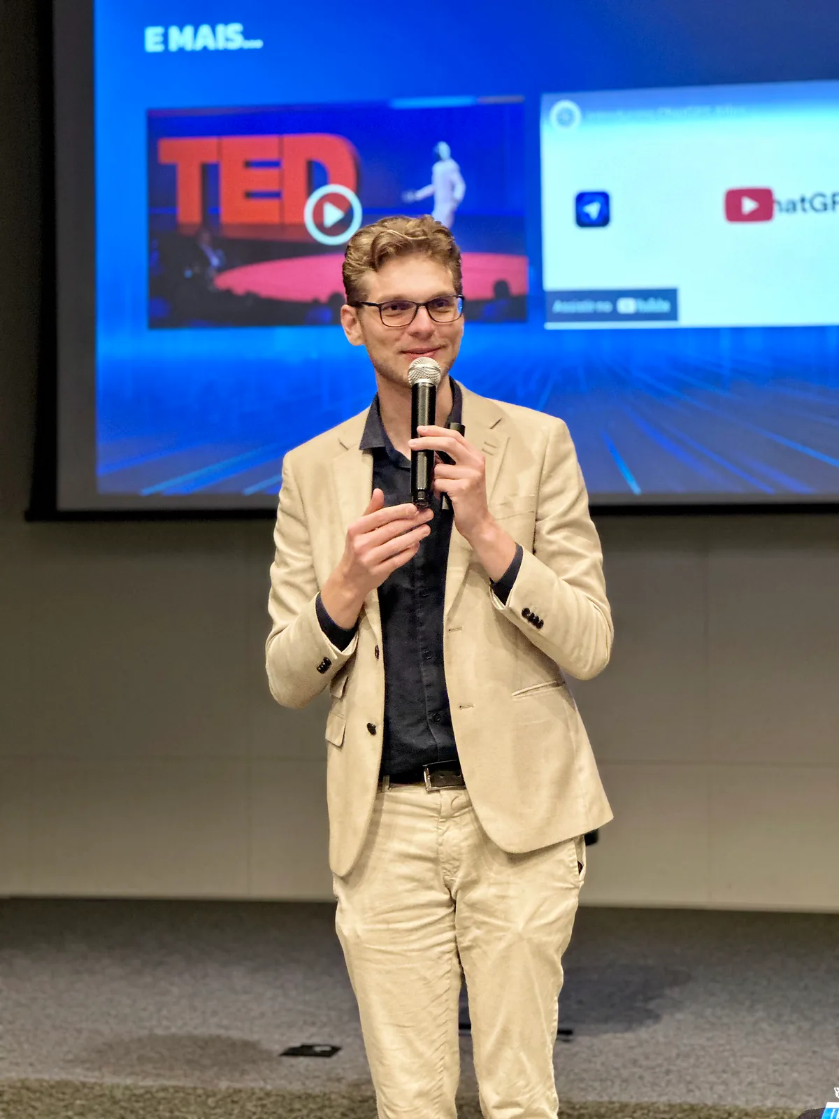 Ricardo Werlang ao microfone na Imersão Pontua, terno bege, telão ao fundo.