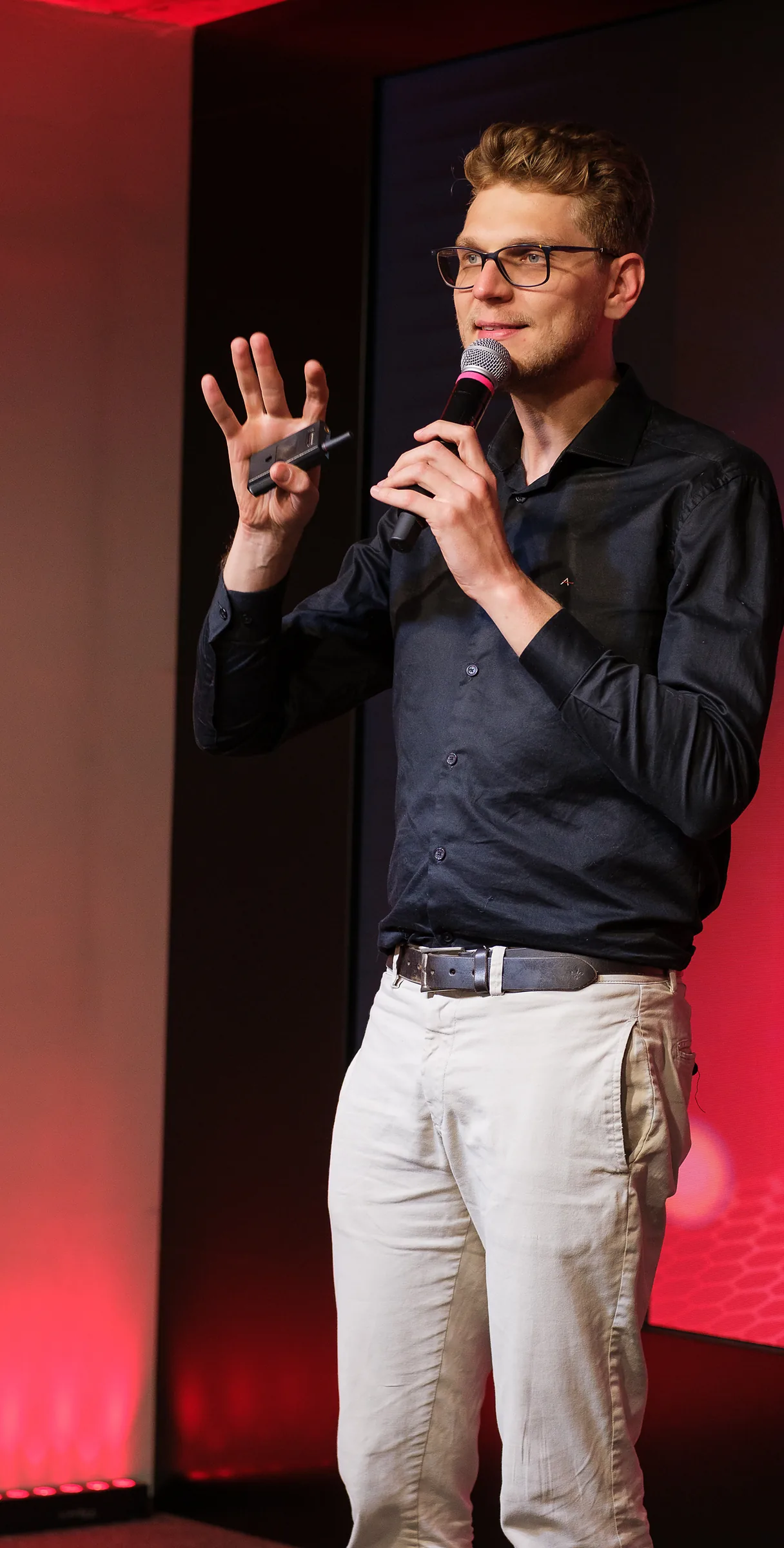 Ricardo Werlang em palestra, microfone na mão, telão vermelho ao fundo.
