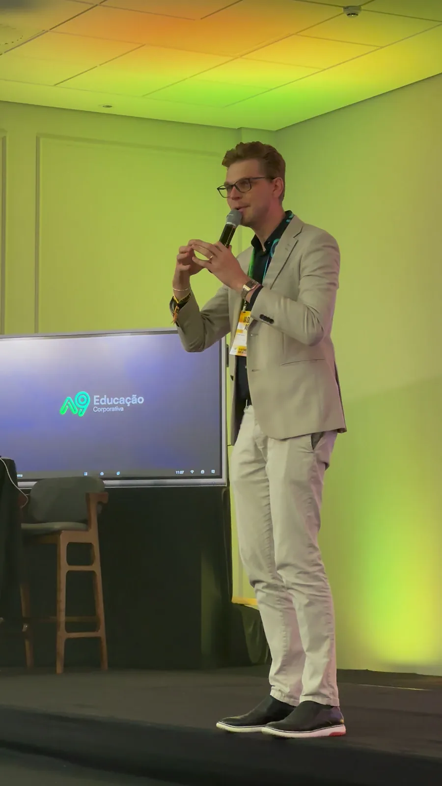 Ricardo Werlang de corpo inteiro no palco do IA Summit A9 2026, tela da A9 Educação Corporativa ao fundo.